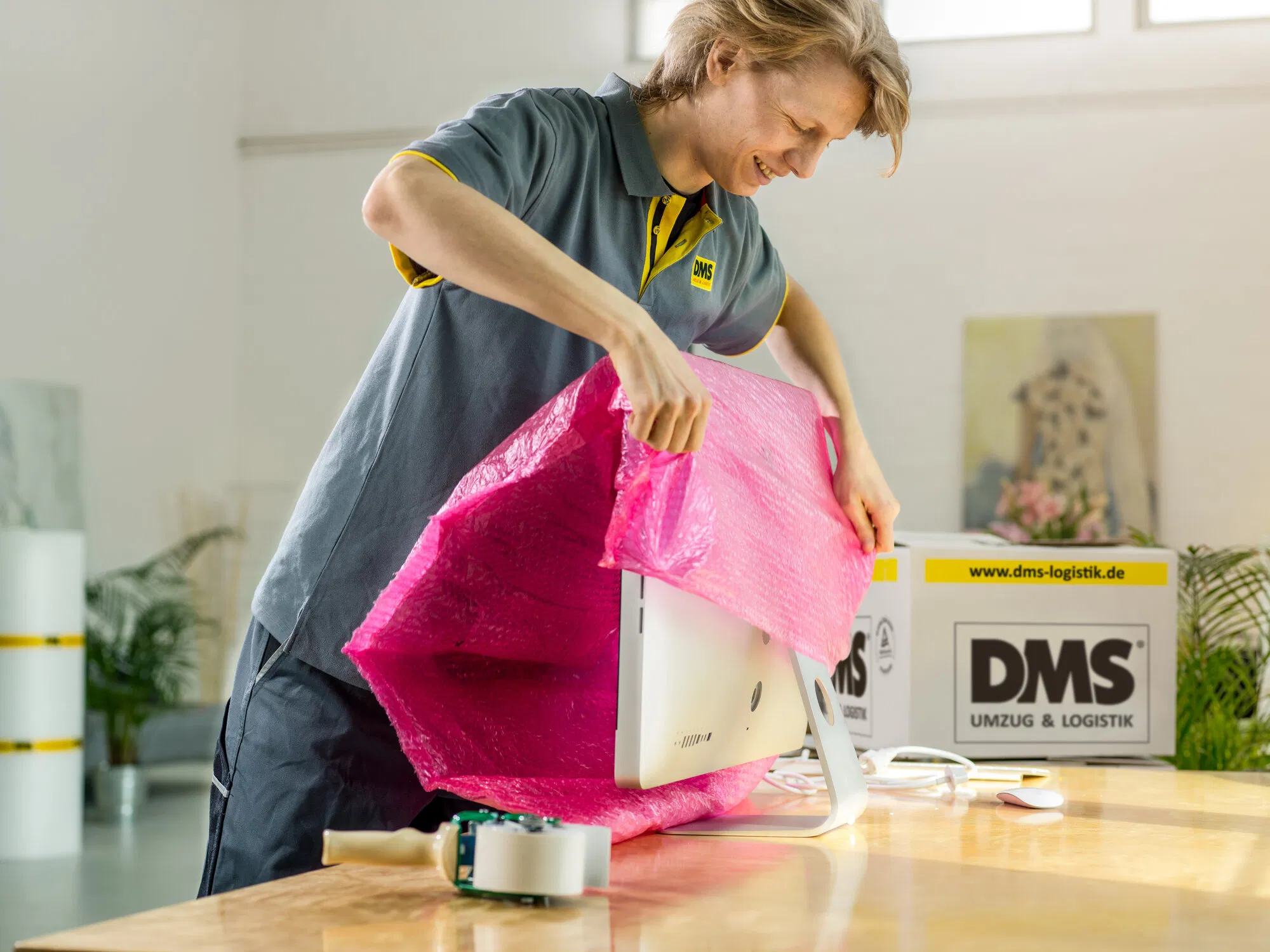 Mitarbeiterin zieht eine pinke Schutzhülle über einen Bildschirm auf einem Tisch.