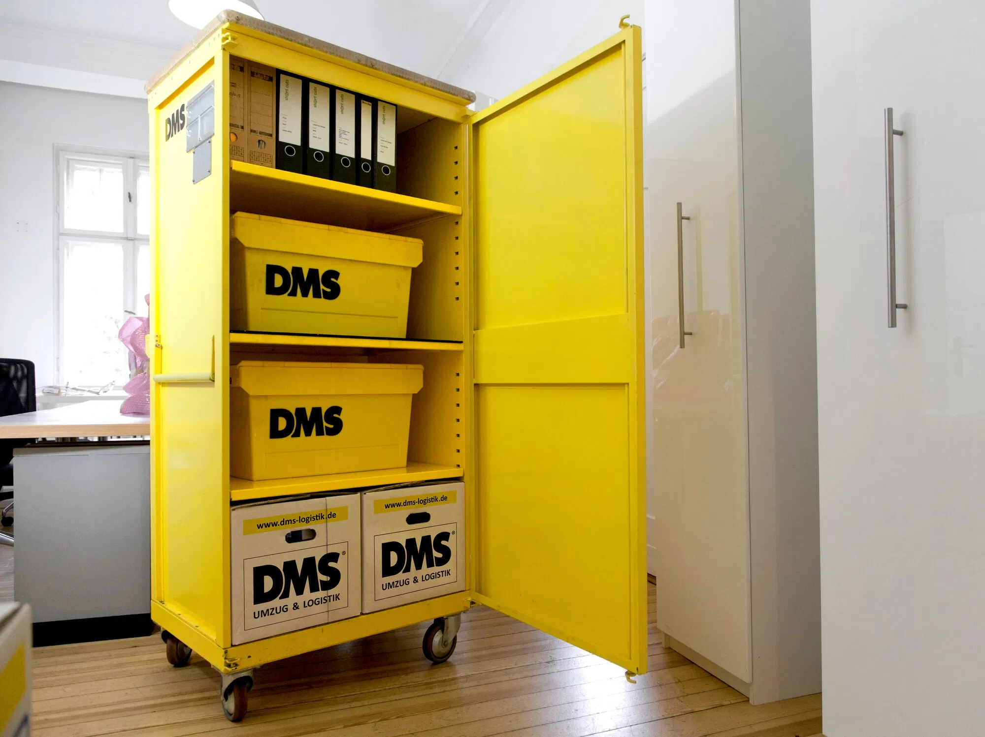Gelber rollbarer Transportschrank mit Aktenordnern und gestapelten Transportboxen.