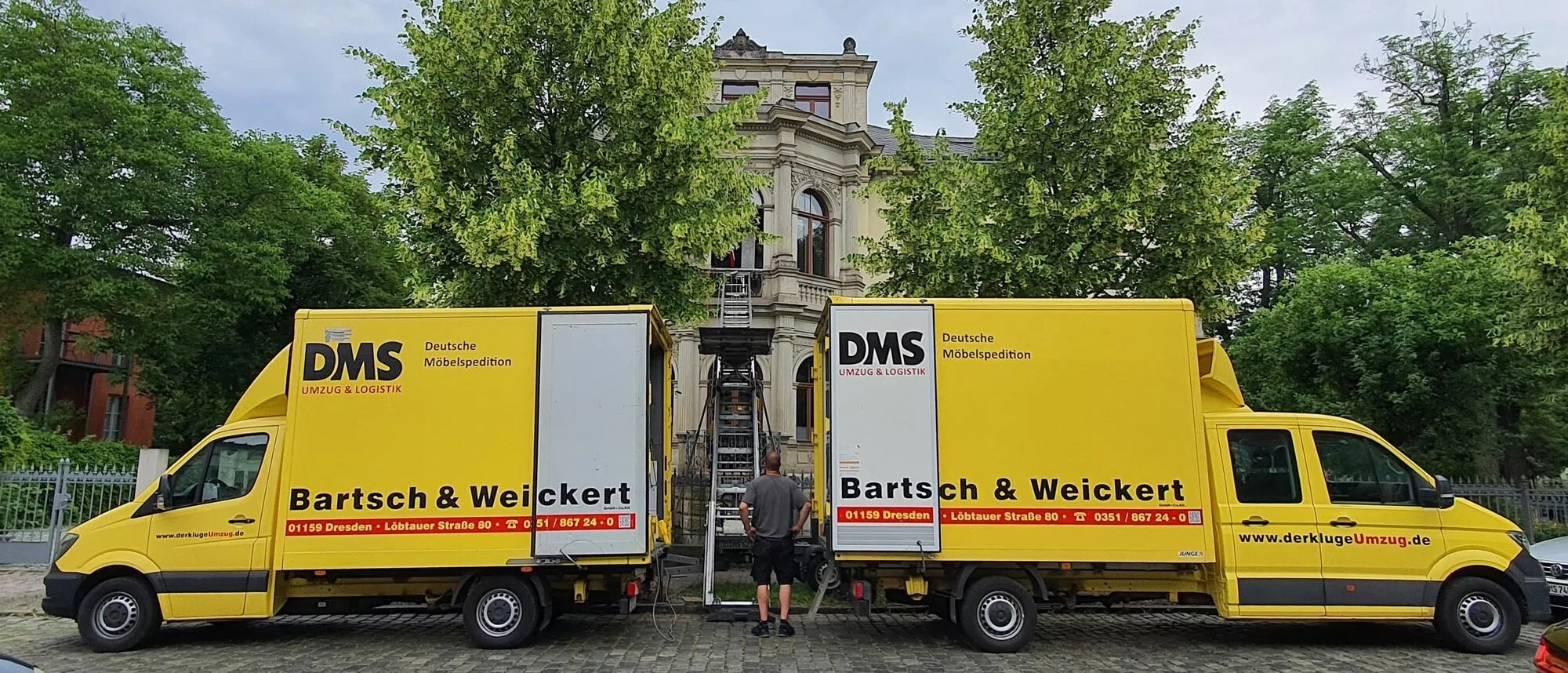 Zwei gelbe Umzugstransporter von Bartsch & Weickert mit Möbellift vor einem Wohnhaus.