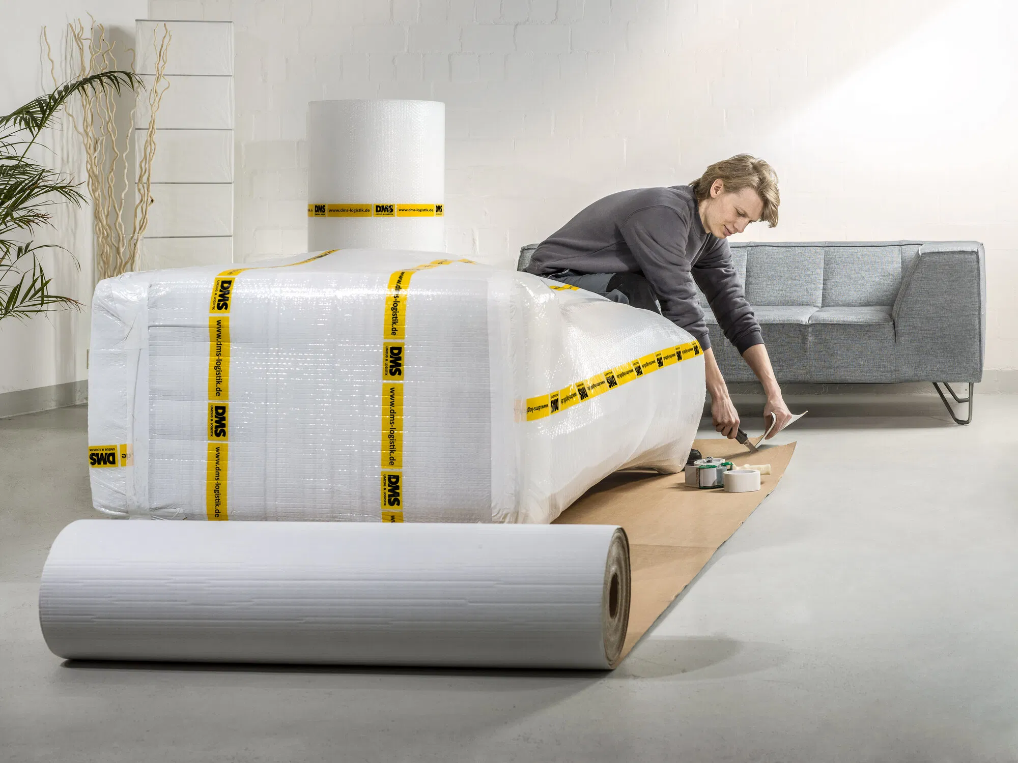 Mitarbeiter bereitet ein Sofa mit Schutzmaterial für den Transport vor.